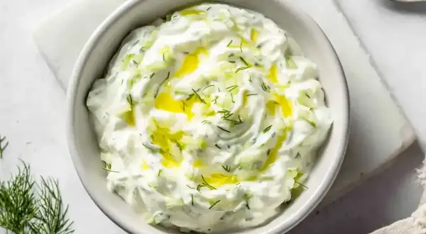 En skål med krämig dip sås med gurka och dill, toppad med olivolja. Perfekt till grillat eller som tillbehör.