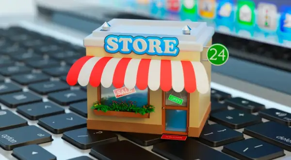 Miniatura de una tienda en línea sobre un teclado de portátil. La tienda tiene un letrero de "STORE", toldo a rayas y un cartel de "OPEN".