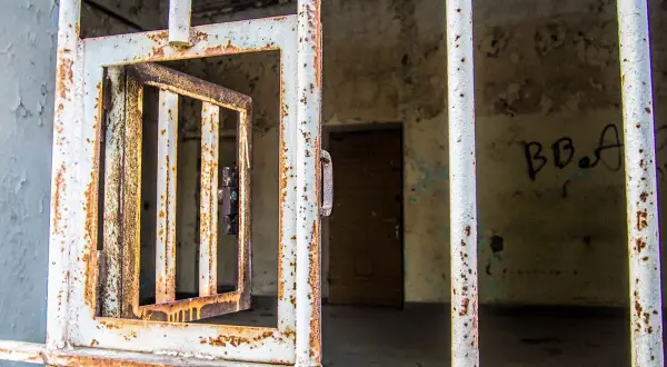 Grille rouillée d'une cellule abandonnée, porte ouverte. Un vestige de l'urbex à Laval, où le passé murmure.