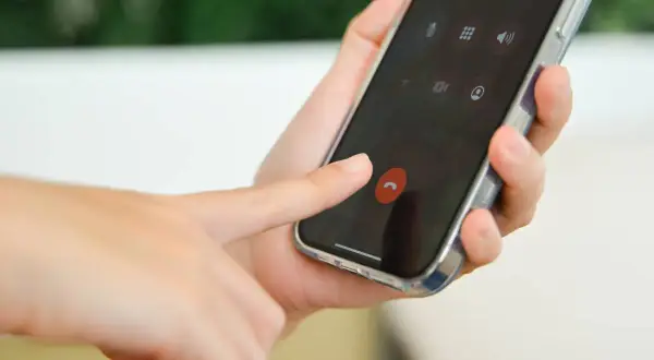 Dłoń naciska czerwony przycisk zakończenia rozmowy na ekranie smartfona, przypominając o kultowych dzwonkach na telefon.