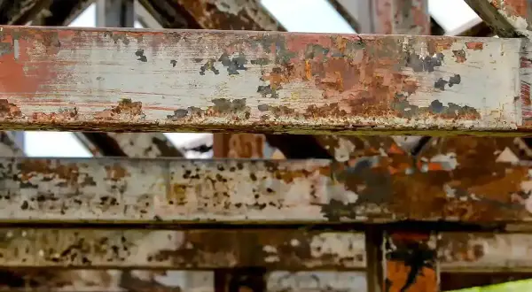 Metalowe belki konstrukcji pokryte rdzą i łuszczącą się farbą. To przykład tego, co to jest korozja, niszcząca metal.
