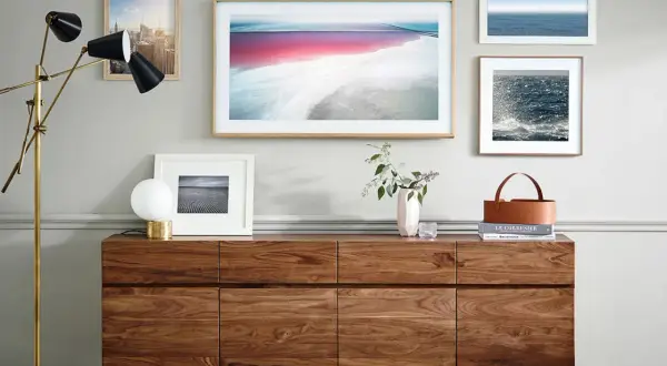 Ein moderner Wohnzimmerschrank aus Holz, der Kunstwerke und einen stilvollen Lampenständer präsentiert. Der große Bilderrahmen in der Mitte könnte einen **Fernseher verstecken**.