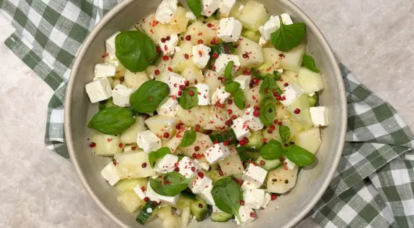 En uppfriskande melonsallad med honungsmelon, fetaost, gurka och basilika, toppad med rosa pepparkorn.