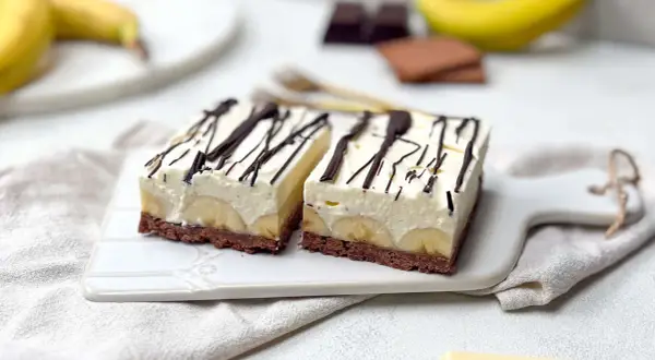 Zwei Stücke Bananensplit Torte mit Schokoladenboden, Bananenscheiben und cremiger Füllung, garniert mit Schokoladensauce.