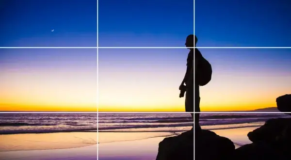 Sylwetka fotografa na tle zachodu słońca, z księżycem na niebie. Kompozycja zgodna z zasadami fotografii, z liniami siatki.