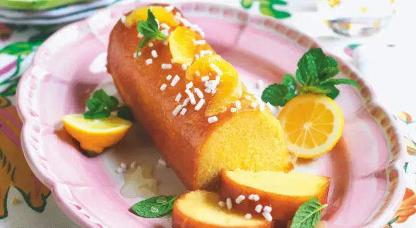 Torta facile glassata all'arancia, decorata con spicchi d'arancia, menta e zuccherini. Servita su un piatto rosa con spicchi di limone.