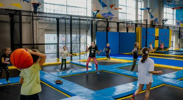 Dzieci skaczą na trampolinach, rzucają piłką i grają w gry. Wspaniałe zabawy na 30 urodziny w parku trampolin.