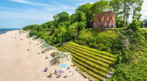 Piękny klif w Trzęsaczu z ruinami kościoła na szczycie. Piaszczysta plaża z wypoczywającymi ludźmi poniżej.