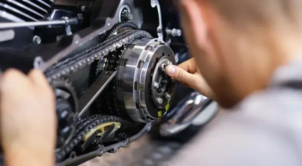 Mechanik naprawia sprzęgło motocykla, widoczny mechanizm z łańcuchem i zębatkami.