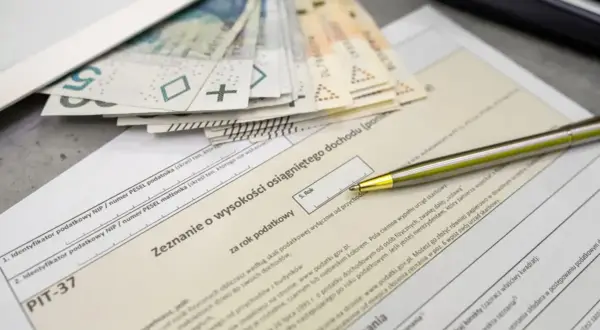 Złożenie PIT-37 z pieniędzmi i długopisem. Zeznanie o wysokości osiągniętego dochodu, pierwszy próg podatkowy.