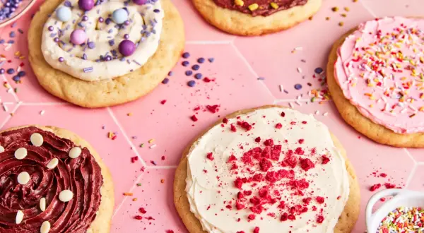 Bunte, verzierte Kekse, darunter ein mit weißer Creme und roten Krümeln bestreuter **crumble cookie**.