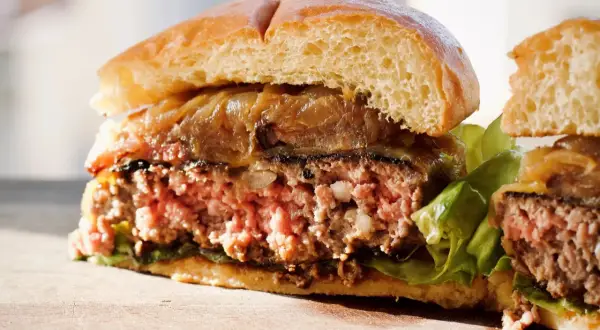 Przekrojony, soczysty burger z karmelizowaną cebulą i sałatą na desce.