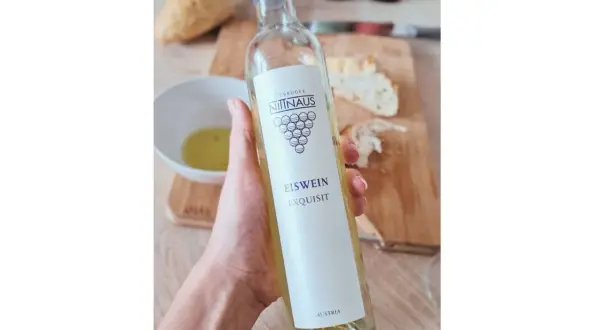 Dłoń trzyma butelkę lodowego wina Eiswein Exquisit z Austrii. Na stole leży chleb i miseczka z oliwą.