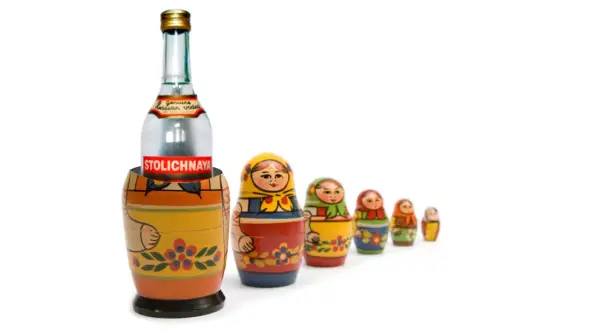 Butelka wódki Stolichnaya w drewnianej babuszce, otoczona mniejszymi matrioszkami.