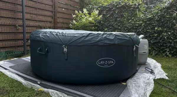 Nadmuchiwane jacuzzi Lay-Z-Spa Miami w ogrodzie, przykryte ciemnozieloną plandeką.
