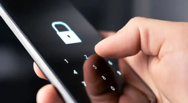Dłoń wpisuje kod na ekranie telefonu, symbolizując jak zmienić kod w domofonie w bloku.
