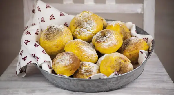En skål med gyllene julgodis med saffran, pudrade med florsocker, på en duk med mönster.