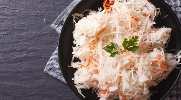 Ein Teller mit traditionellem Sauerkraut-Rezept, garniert mit Petersilie und Karottenstreifen, auf dunklem Stein serviert.