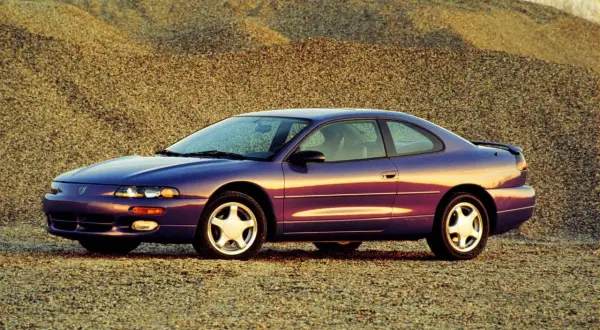 Fioletowy Dodge Avenger z lat 90. stoi na tle żwirowych wzgórz.