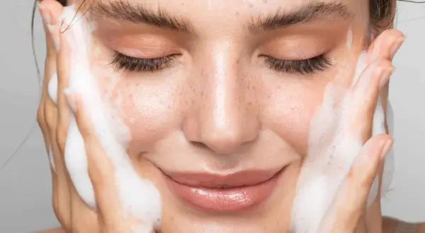 Visage de femme aux yeux fermés, profitant d'un nettoyage en profondeur avec de la mousse sur les joues.