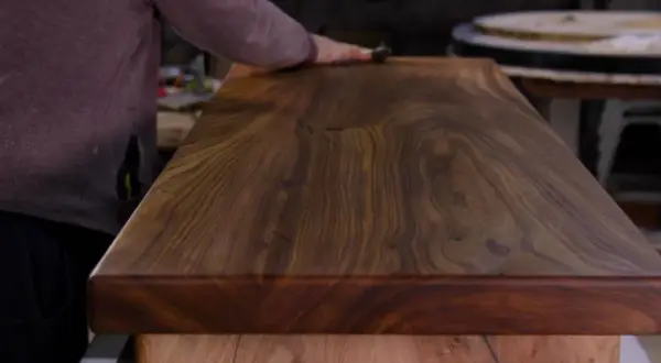 Main d'artisan polissant un plateau en bois exotique pour un entretien intérieur parfait.
