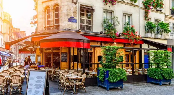 Un caffè parigino con tavolini all'aperto, fioriere rigogliose e un'atmosfera accogliente. Il dehors, in questo contesto, è un invito a godersi la vita.