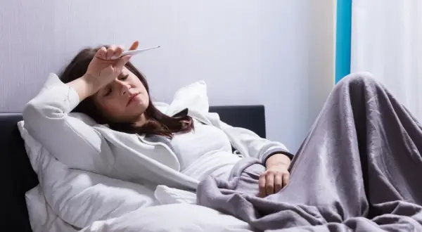 Kobieta z gorączką mierzy temperaturę, marząc o ulgę, którą może przynieść Biseptol 960.