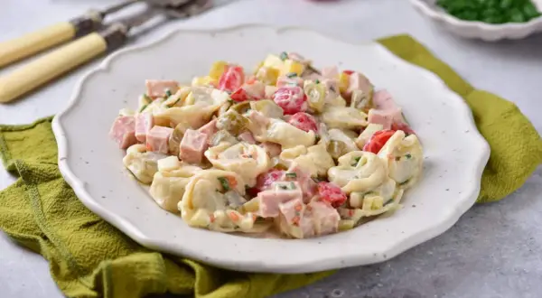 Prosta sałatka z tortellini, szynką, pomidorkami i ogórkiem konserwowym, polana kremowym sosem.