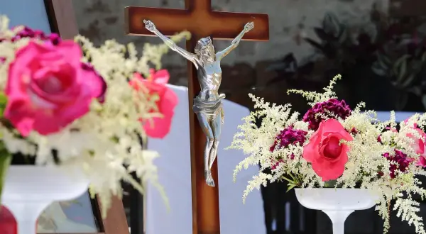Drewniany krzyż z figurą Chrystusa, otoczony bukietami róż i białych kwiatów. Czy zdrada w myślach grzech?