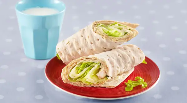 Två saftiga tonfisk wraps med krispig sallad på en röd tallrik, bredvid ett glas mjölk.