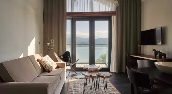 Przytulny pokój z widokiem na jezioro w hotelu Lake Hill Resort & Spa w Karkonoszach. Sofa, stoliki kawowe i krzesło motylkowe tworzą komfortową przestrzeń.