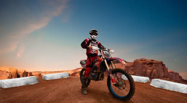 Motocyklista enduro w stroju i kasku na tle pustynnego krajobrazu z klifami i niebem.