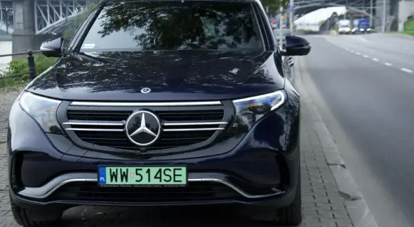 Ciemnoniebieski Mercedes EQC z tablicą rejestracyjną WW 514SE zaparkowany przy ulicy, w tle most.