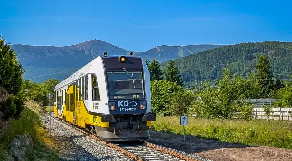 Pociąg KD jedzie po torach w kierunku gór. Widok na Karkonosze, idealny na podróż ze Szklarskiej Poręby do Karpacza PKP.