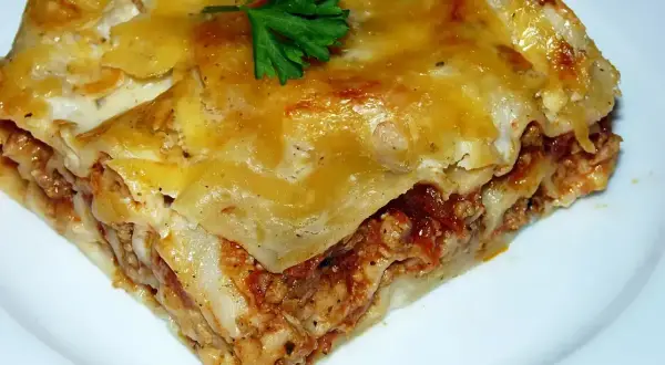 Pyszny kawałek lasagne z mięsem mielonym, zrumieniony ser i świeża natka pietruszki. Idealny przepis na obiad.