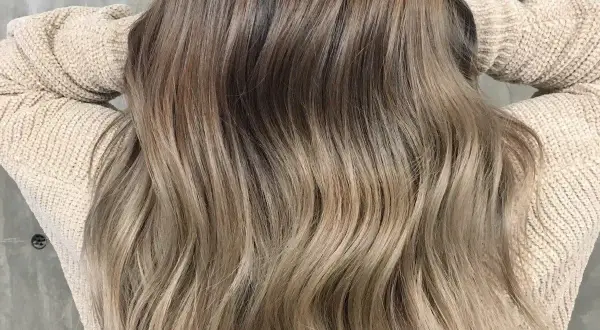 Piękne, długie włosy w odcieniu naturalny ciemny blond z refleksami, delikatnie pofalowane, opadające na beżowy sweter.