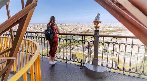 En kvinna med ryggsäck njuter av utsikten över Paris från Eiffeltornet. Hon undrar nog hur många trappsteg har Eiffeltornet.
