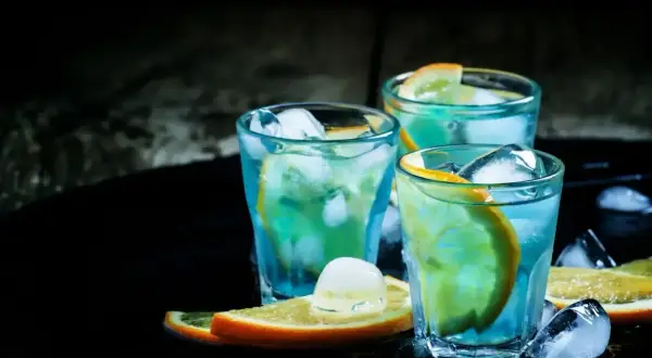 Trzy orzeźwiające drinki z blue curacao, ozdobione plasterkami pomarańczy i kostkami lodu, kuszą swoim tropikalnym kolorem.