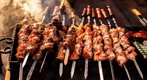 Rader av saftiga köttspett grillas över glöd. Röken stiger och doften lovar något gott att grilla.
