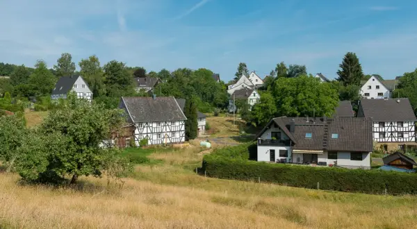 Fachwerkhäuser säumen den malerischen fachwerkweg Ruppichteroth, eingebettet in grüne Hügel unter blauem Himmel.