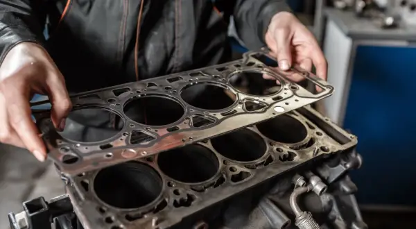 Mechanik przygotowuje wymianę uszczelki pod głowicą silnika. Nowa uszczelka czeka na montaż.