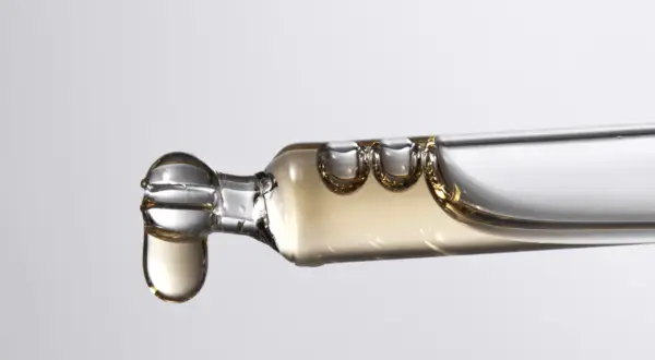 Tropfen eines goldenen Serums, das Bisabolol enthält, fallen aus einer Pipette.
