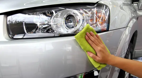 Ręka z zieloną mikrofibrą poleruje reflektor srebrnego samochodu. To praca detailera, który dba o każdy szczegół.