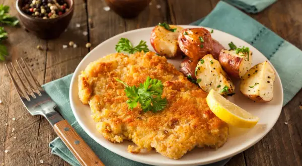 Goldbraunes Schnitzel, perfekt paniert, mit Rosmarinkartoffeln und Zitrone. So paniert man Schnitzel für ein köstliches Essen.