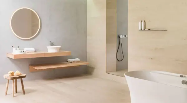 Baño moderno con lavabo flotante, bañera blanca y ducha. El suelo de madera clara contrasta con los azulejos de la pared.