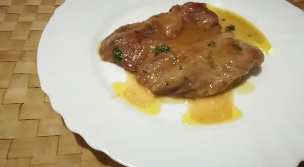 Due fettine di tacchino appetitose, immerse in una salsa dorata e profumata, servite su un piatto bianco.