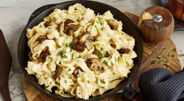 Cremiges Pasta Alfredo mit Pilzen, garniert mit Petersilie, serviert in einer Gusseisenpfanne.