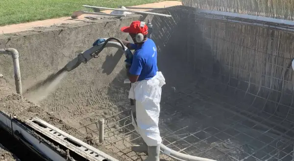 Un ouvrier projette du béton pour créer un bassin en béton étanche. La structure métallique est visible.