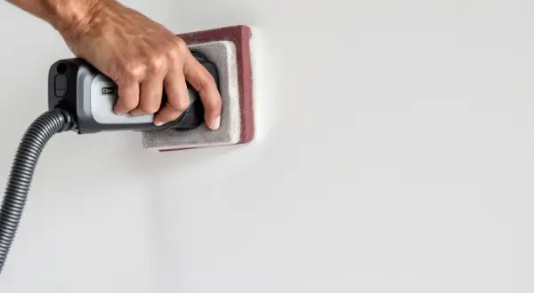 Main tenant utilise un aspirateur pour nettoyer le mur après ponçage.