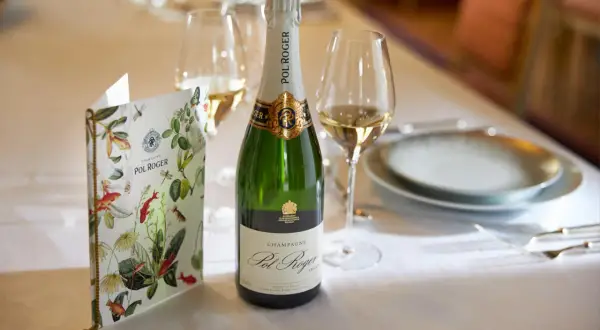 Eine Flasche Pol Roger Champagner steht bereit, daneben ein Glas und eine Speisekarte mit floralem Muster.